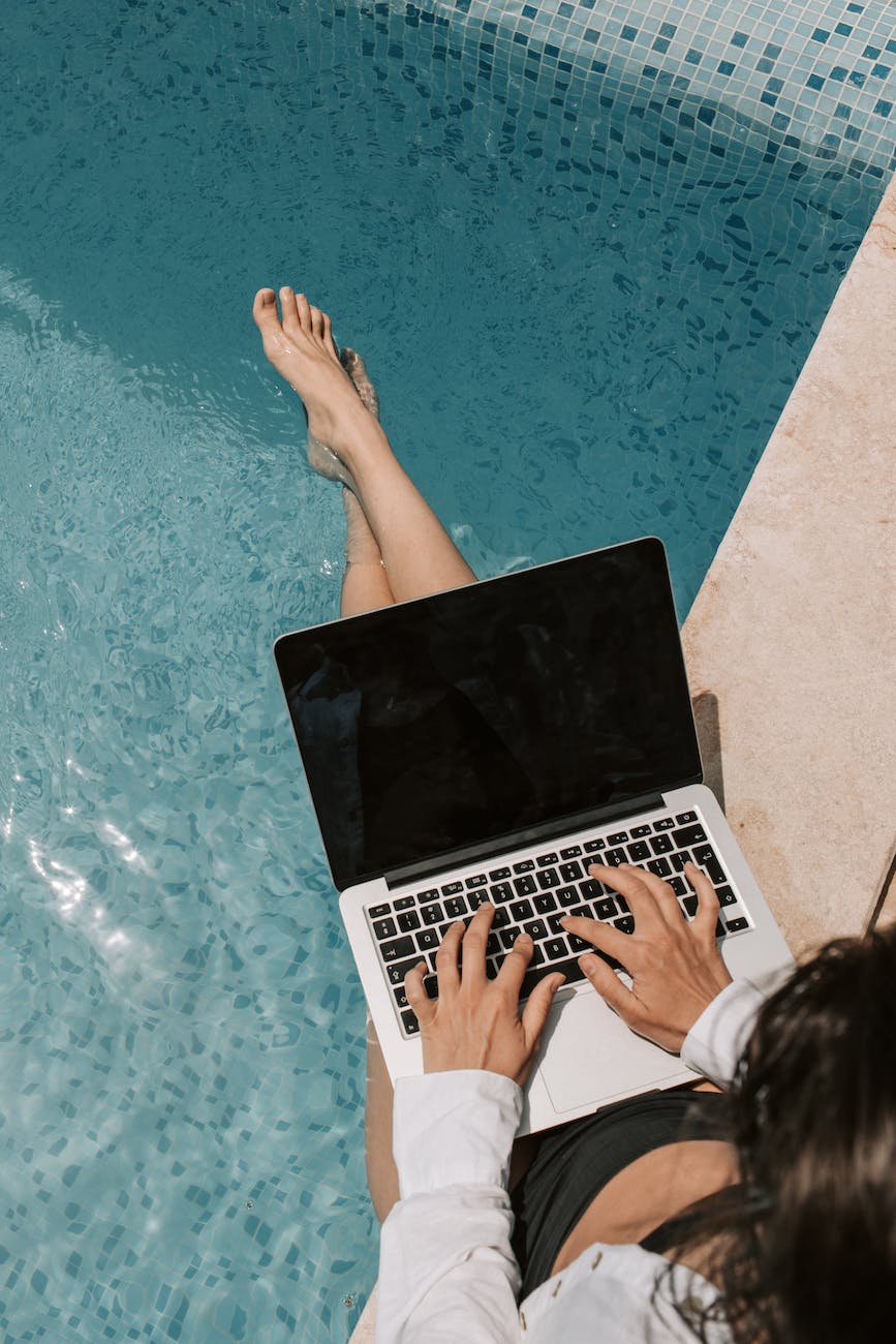Woman optimizing SEO for swimming pool businesses on laptop by poolside.